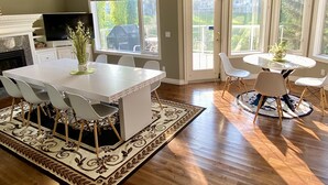 A spacious dining area with a white table and chairs, a patterned rug, and large windows offering views of greenery. - Ravine House, 4000sqf, View, AC,Sleep12+

 (Calgary)