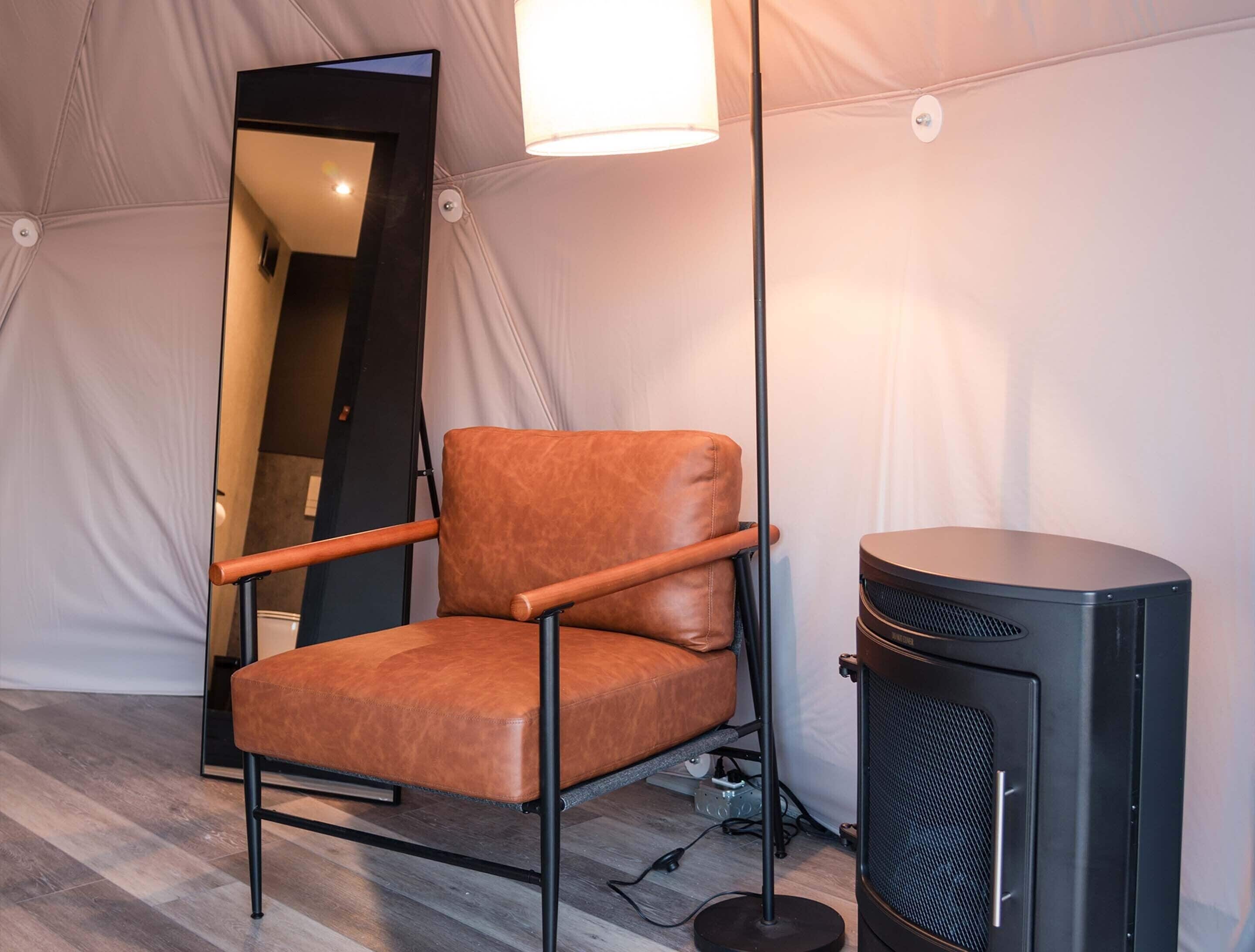 A chair with a high backrest and armrests, positioned next to a black speaker and a floor lamp.