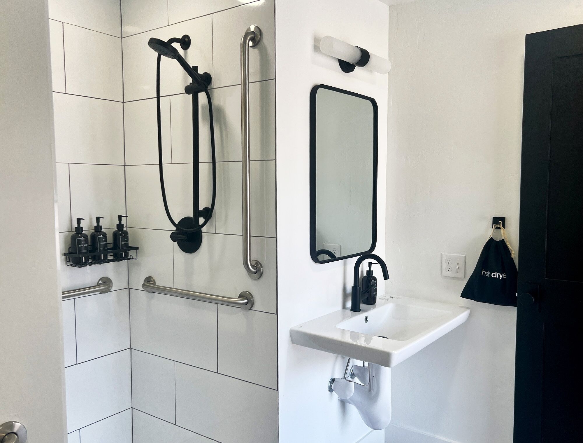 A modern bathroom with a walk-in shower, grab bars, a sink, and a mirror.