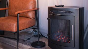 Quarto com uma poltrona de couro, um aquecedor preto com grade frontal e um cabo elétrico no chão.