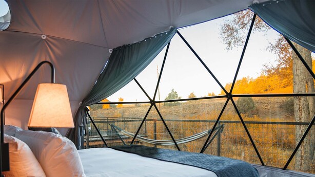 A bedroom with a large window, a hammock, and a bed with pillows.