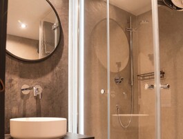 Un baño moderno con un espejo redondo, un lavabo blanco y una zona de ducha con mampara de vidrio.
