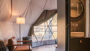 A tented room with a hammock, a chair, a lamp, and a bathroom with a sink and mirror.