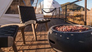 A wooden deck with a black woven chair, a white tent, and a grill with charcoal.