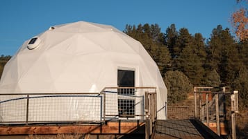 A dome-shaped structure with a door and a small window, surrounded by a wooden deck and metal fencing.