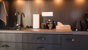 A modern kitchen with dark wood cabinets, a stainless steel faucet, a kettle, a coffee maker, and a countertop with a paper towel dispenser.