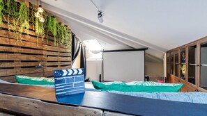 Una habitación con pared de listones de madera, plantas colgantes, una pantalla de proyector y una claqueta sobre una mesa.
