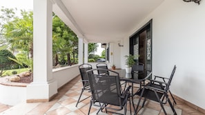 Un patio cubierto con una mesa y sillas, rodeado por un muro blanco y vistas a zonas verdes.