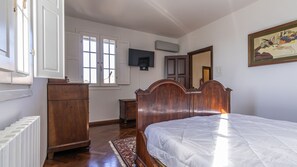 A bedroom with a wooden bed, a dresser, a radiator, a television, and a window with blinds.