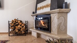 A fireplace with a fire, a stack of firewood, and a decorative wall piece.
