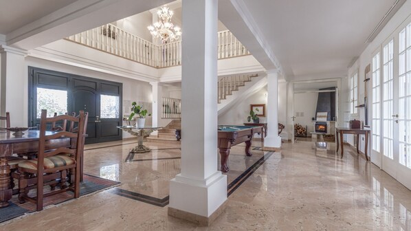A spacious interior with a pool table, dining area, and a staircase leading to an upper level.