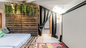 A bedroom with a bed, wooden slat wall, hanging plants, a black curtain, and a red patterned rug. - Villa Petrone | Luxury Home-Wi-Fi,Biliardo,Jacuzzi (Emilia-Romagna)