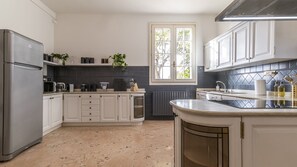 A kitchen with white cabinets, a refrigerator, a window with a view, and a countertop with various items.