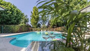A swimming pool with a glass table and chairs, surrounded by greenery and a hedge. - Villa Petrone | Luxury Four Seasons-Jacuzzi&Pool (Emilia-Romagna)