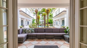 A covered outdoor seating area with a cushioned bench, a hammock, and a view of a pool and palm trees. - Villa Petrone | Luxury Home-Wi-Fi,Biliardo,Jacuzzi (Emilia-Romagna)