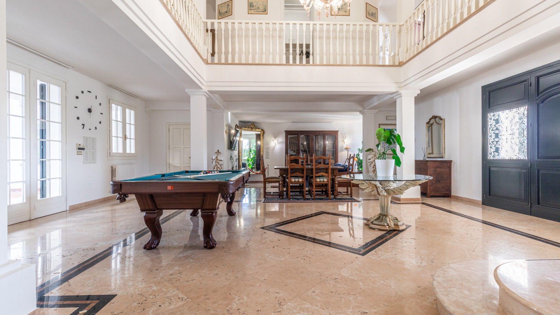 Une pièce spacieuse comprenant une table de billard, un coin repas agrémenté d’un lustre et un grand miroir.