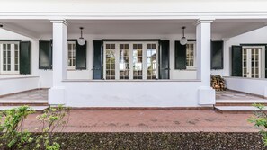 A white building with a covered porch, green shutters, and a tiled entrance.