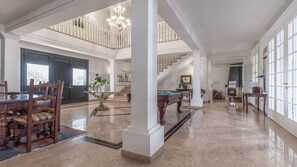 Amplia sala de estar con mesa de billar, comedor y una escalera que sube a un nivel superior.