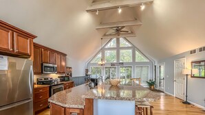 A spacious kitchen with a large island, wooden cabinets, stainless steel appliances, and a high ceiling with skylights.