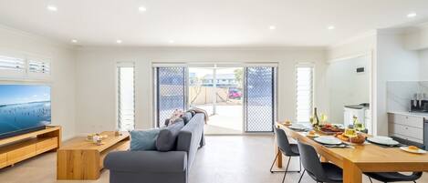 A modern living room with a sofa, TV, and dining area with a table set for two.