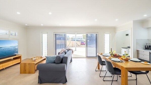Una sala de estar moderna con un sofá, televisor y comedor con una mesa dispuesta para dos personas.