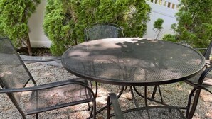 Une table ronde en métal, entourée de quatre chaises, et bordée de gravier et d’arbres.