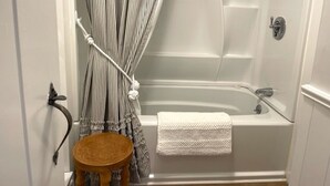 Une salle de bain avec une baignoire, un tabouret en bois et un rideau de douche à rayures.