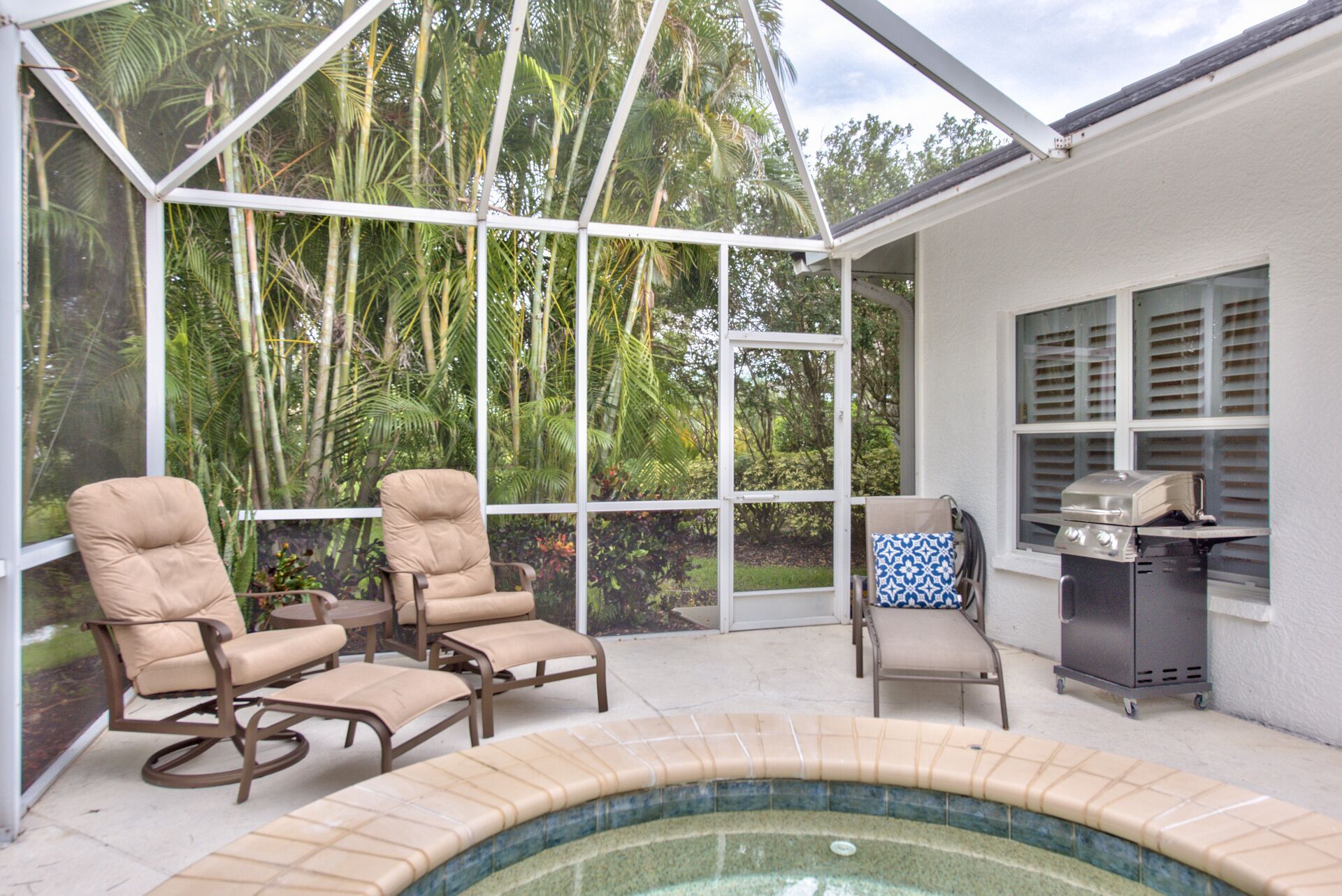 A covered outdoor area with a hot tub, lounge chairs, and a grill.