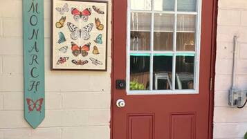 A red door with a glass window, a 'mini MONARC' sign, and a framed butterfly artwork on a beige wall.
