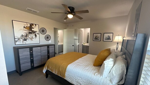 Un dormitorio con cama, ventilador de techo, cómoda y obras de arte en las paredes.