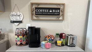 Una encimera de cocina con cafetera, molinillo de café, tostadora y cartel de barra de café.