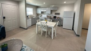 Una cocina moderna con armarios blancos, una mesa de comedor con sillas, un refrigerador y un microondas.