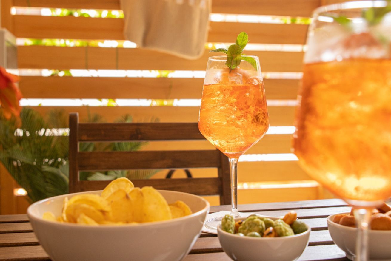 A table with a drink in a glass, a bowl of chips, and a bowl of guacamole.