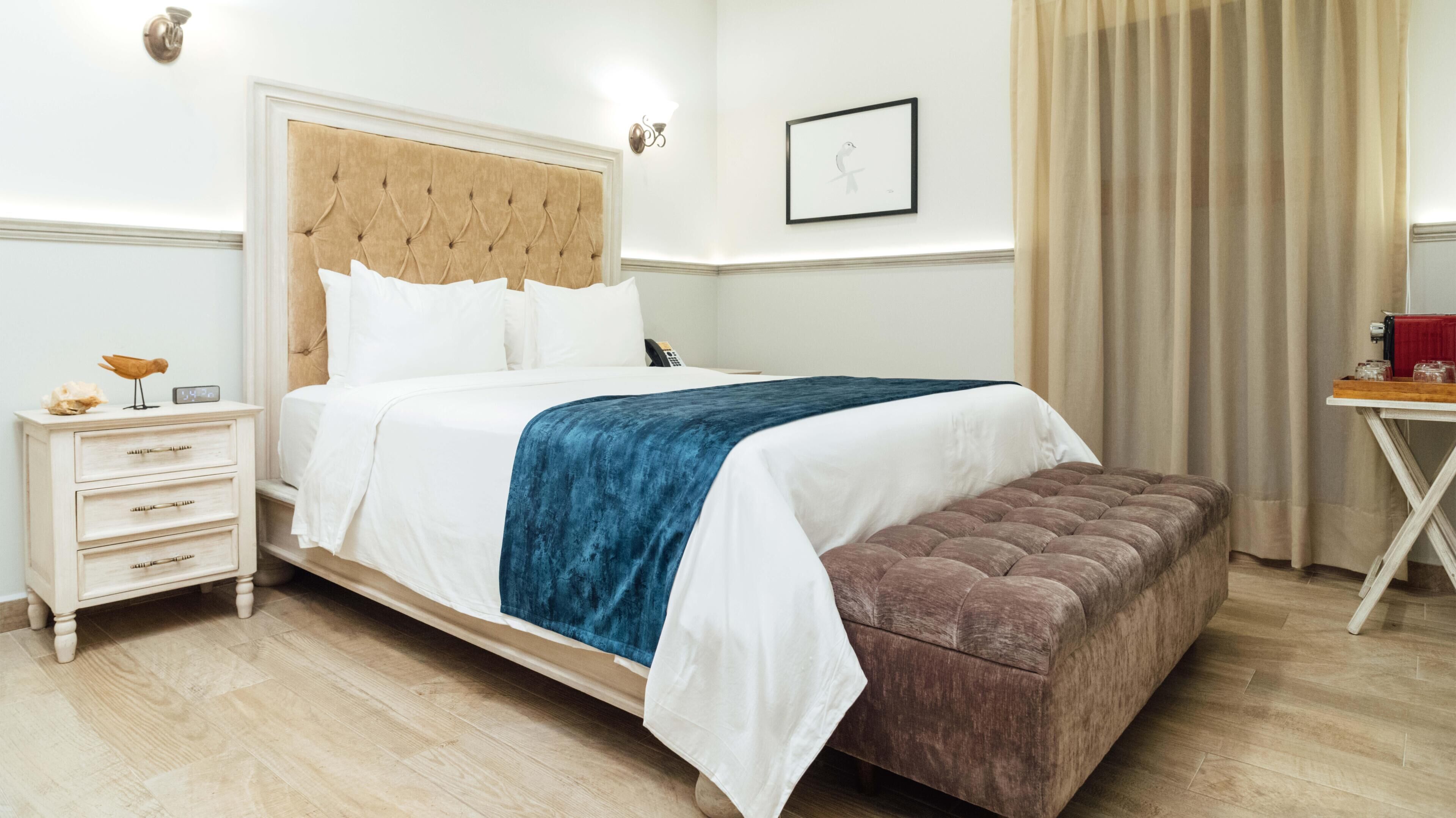Une chambre d’hôtel bien rangée, avec un lit, une table de chevet et une petite table sur laquelle sont posés divers objets.