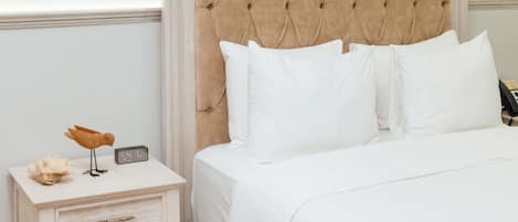 A neatly made bed with white bedding, a wooden nightstand with a clock, and a decorative bird sculpture.