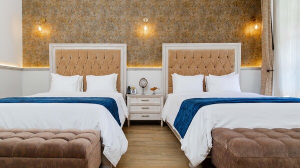 Habitación de hotel con dos camas, una mesita de noche, suelo de madera y papel tapiz estampado.