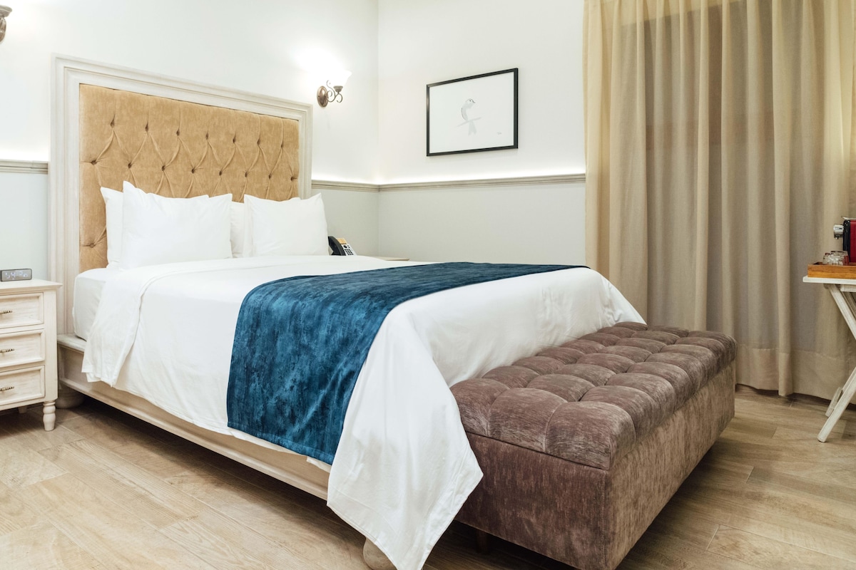 A neatly arranged hotel room with a bed, bedside table, and a small table with items on it.