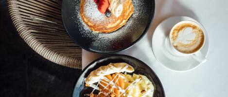A breakfast setting with pancakes, berries, and a cup of coffee on a table.