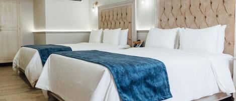 A hotel room with two beds, a large padded headboard, a wooden floor, and a wall-mounted air conditioner.