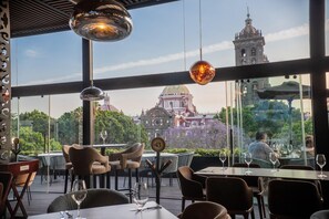 An outdoor dining area with tables and chairs, a view of a historic building, and hanging pendant lights. - Voco Royalty Puebla Downtown (Puebla)