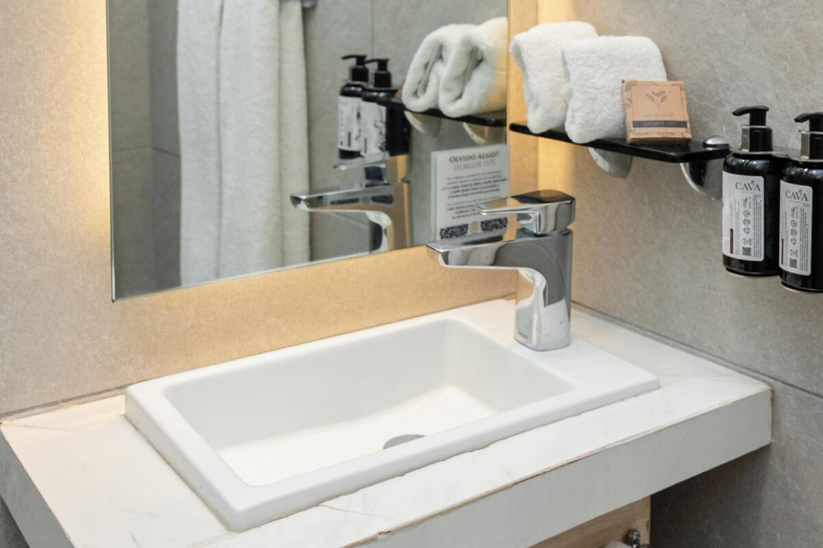 A bathroom with a white sink, a mirror, a towel rack, and two black bottles of hand soap.