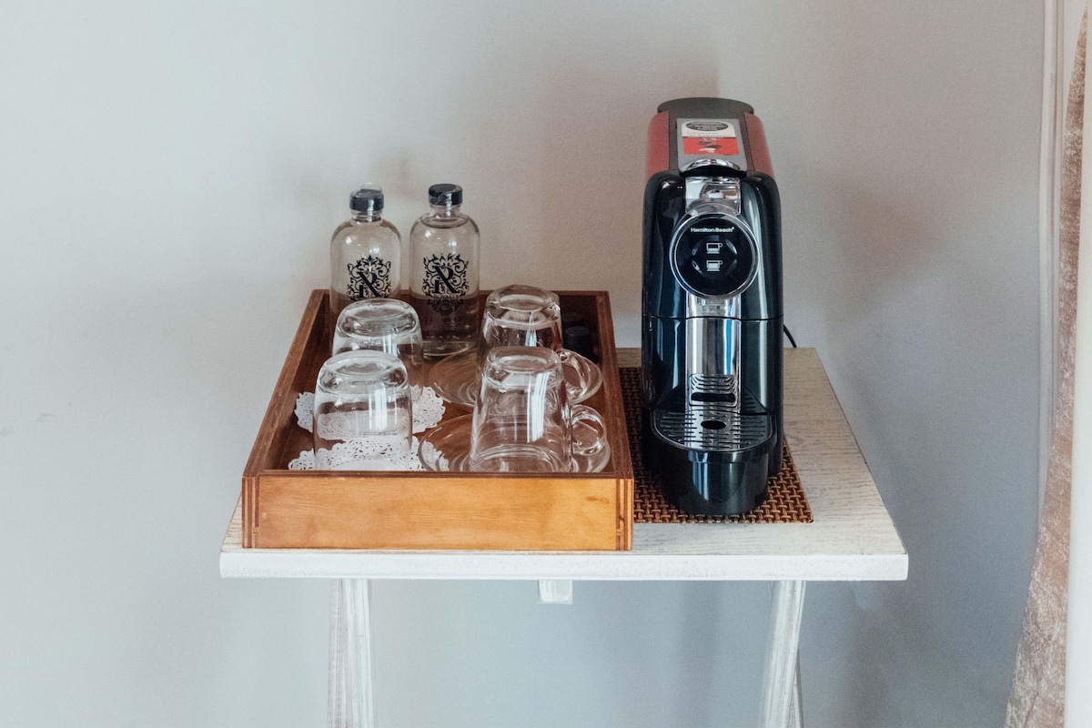 A coffee maker, two bottles, and a tray with glassware on a table.