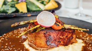 A plate of food with a piece of meat, vegetables, and sauce. - Voco Royalty Puebla Downtown (Puebla)