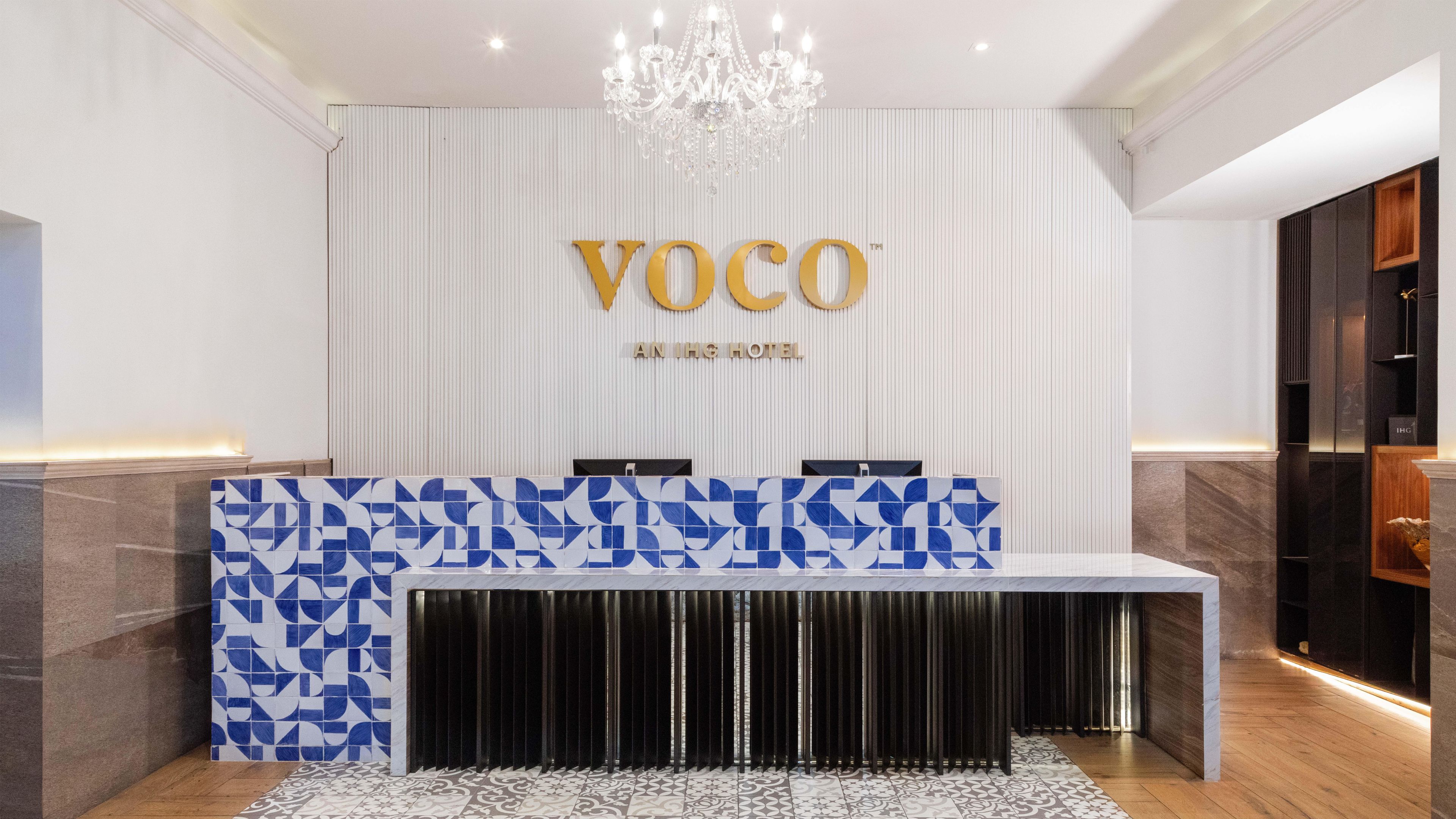 Ein Empfangsschalter mit modernem Design, eine Chandelüster und ein Schild mit der Aufschrift 'VOCO AN ING HOTEL'.