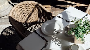 A dining table with a white plate, a fork, a knife, and a cup of coffee. There is a wicker chair and a potted plant on the table. - Voco Royalty Puebla Downtown (Puebla)