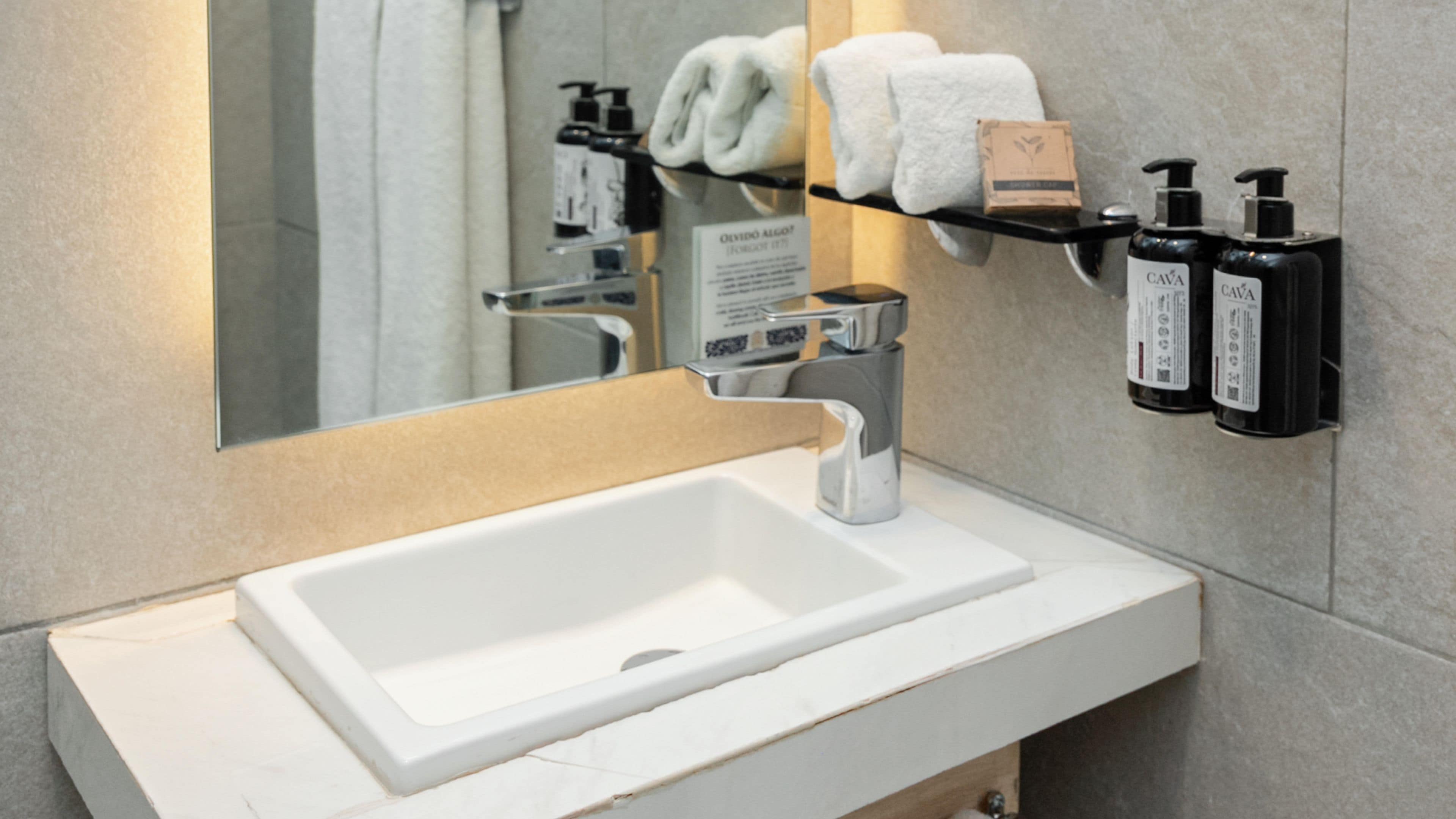 A bathroom with a white sink, a mirror, a towel rack, and two black bottles of hand soap.