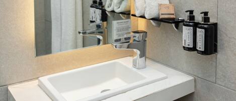 A bathroom with a white sink, a mirror, a towel rack, and two black bottles of hand soap.