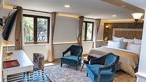 A hotel room with a bed, two armchairs, a desk with a lamp, and a TV. - Voco Royalty Puebla Downtown (Puebla)