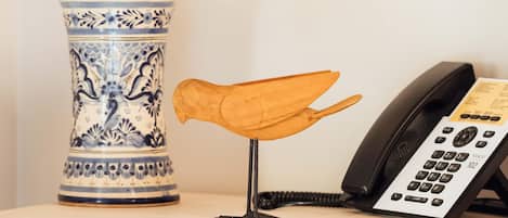 Un jarrón azul y blanco de cerámica, una escultura de pájaro de madera y un teléfono sobre una mesa.