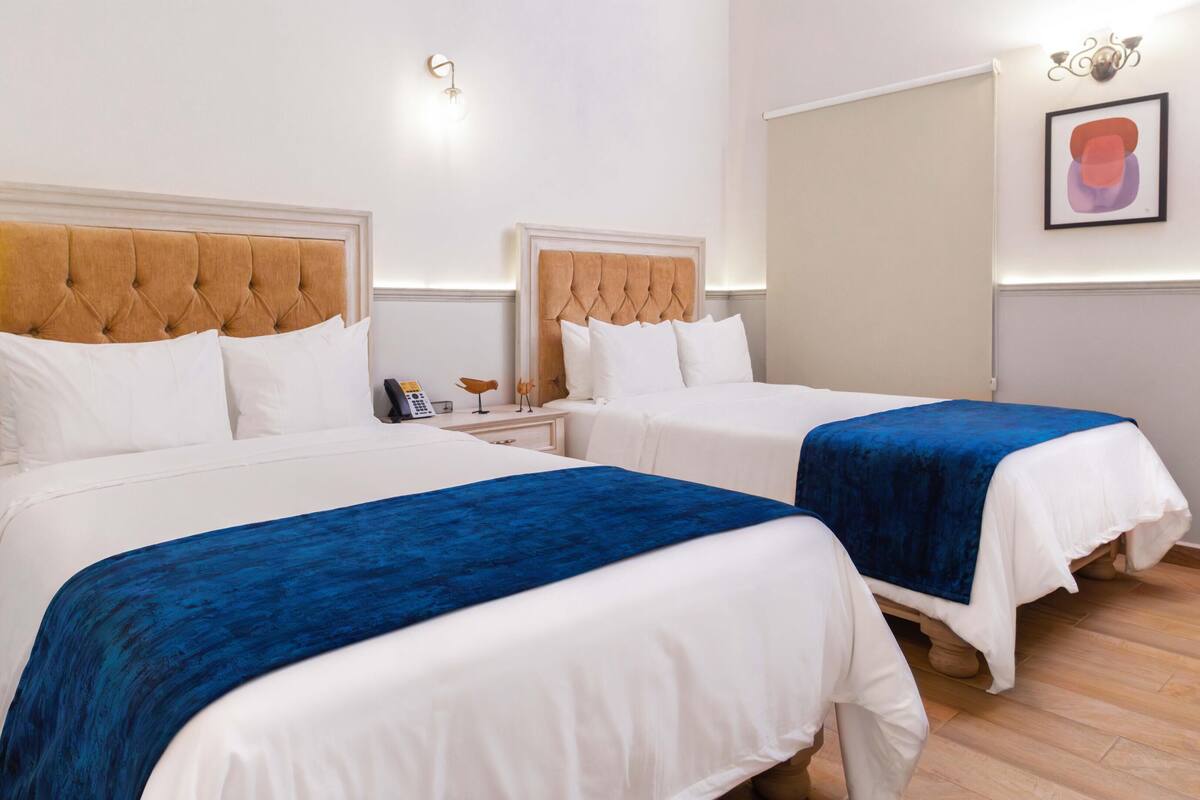 A hotel room with two beds, white bedding, and blue throw blankets.
